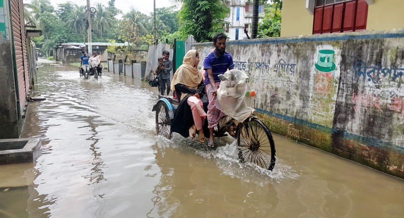 In the photo, residents of Morelganj municipality are seen crossing waterlogged streets daily on Rickshaws-Van and by foot. Locals blame poor and unplanned drainage systems for the persistent flooding caused by continuous rainfall. (Photo: V7N)